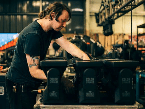 Worker inspecting stage lighting equipment in a workshop.